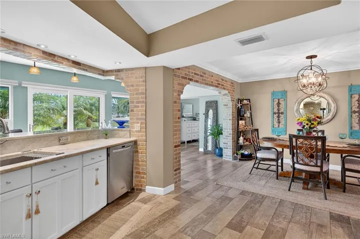 Kitchen with light wood-style floors, stainless steel dishwasher, white cabinets, brick wall, and pendant lighting