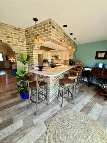 Kitchen with a peninsula, arched walkways, brick wall, light countertops, and a breakfast bar area