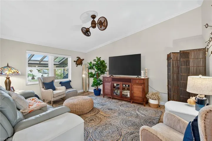 Living room with ornamental molding, vaulted ceiling, and wood finished floors