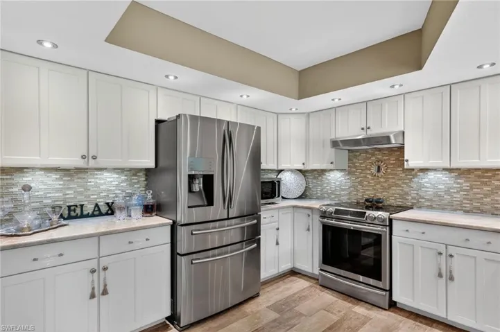 Kitchen with appliances with stainless steel finishes, recessed lighting, white cabinetry, tasteful backsplash, and light wood-type flooring
