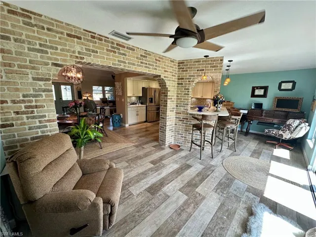 Dining area with a chandelier, brick wall, a ceiling fan, arched walkways, and light wood-style flooring