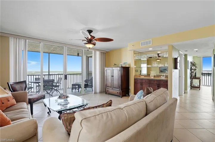 Living room with a wall of windows, light tile patterned flooring, a ceiling fan, and a water view - Virtually Edited Image