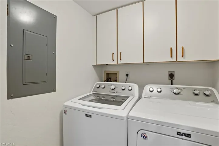 Laundry area featuring electric panel, cabinet space, and washing machine and dryer - Virtually Edited Image