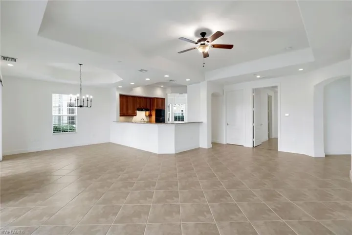 Unfurnished living room with a raised ceiling, light tile patterned floors, and ceiling fan with notable chandelier