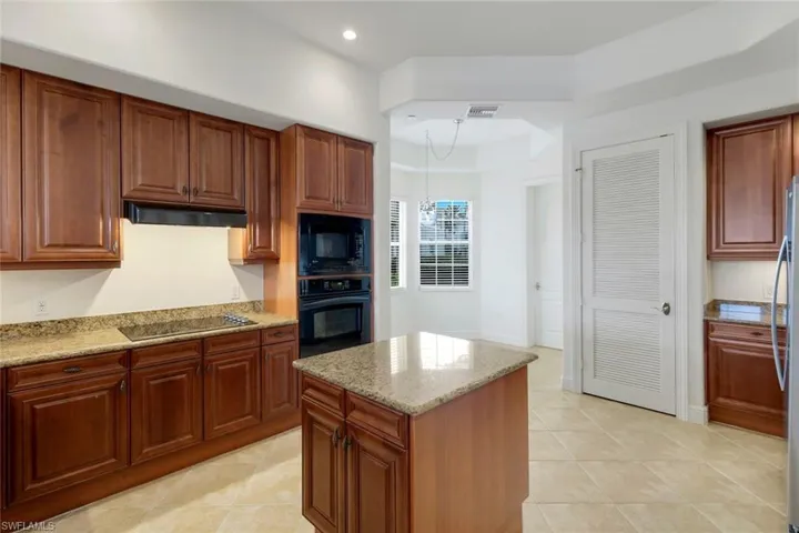 Kitchen featuring an inviting chandelier, light stone counters, pendant lighting, a kitchen island, and black appliances