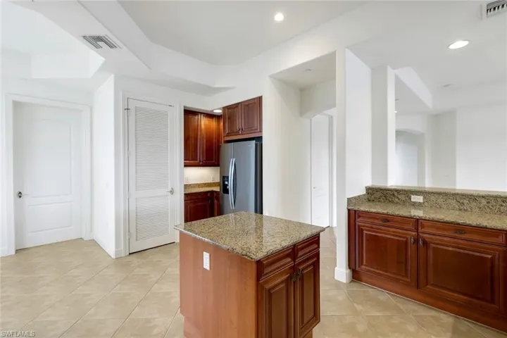 Kitchen featuring stainless steel fridge, light tile patterned floors, light stone countertops, and a kitchen island