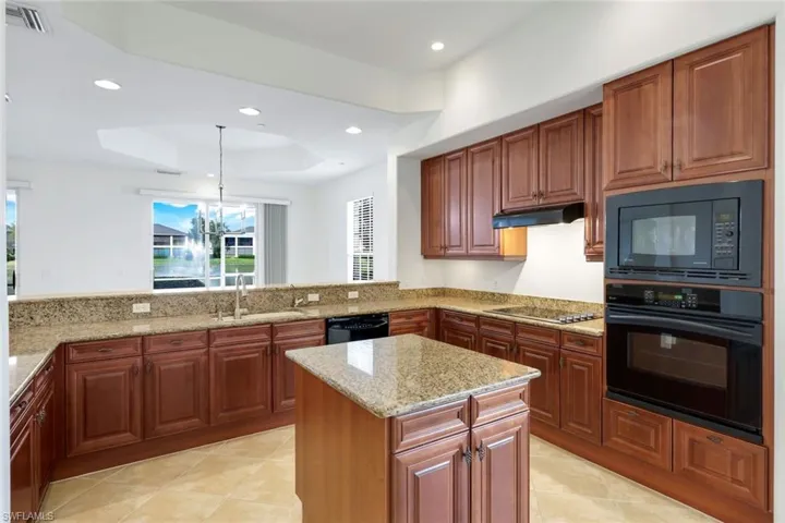 Kitchen with kitchen peninsula, a raised ceiling, sink, black appliances, and hanging light fixtures