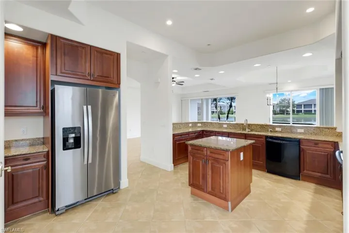 Kitchen with light stone countertops, dishwasher, a center island, and stainless steel refrigerator with ice dispenser