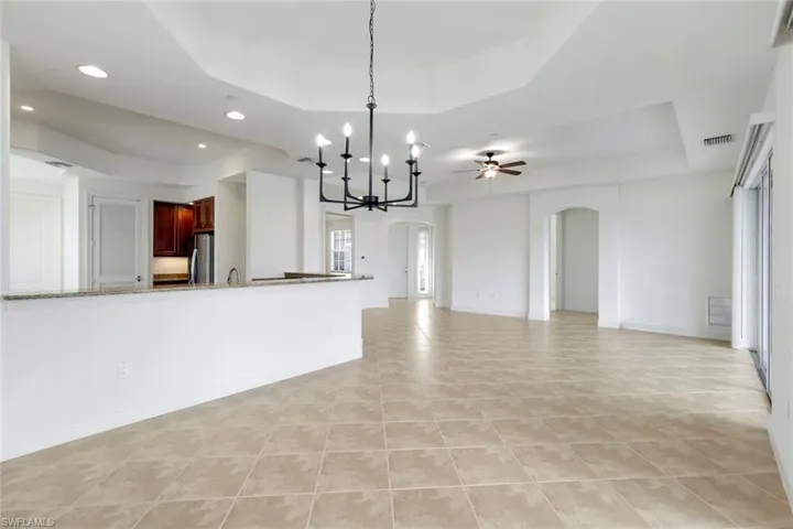 Kitchen featuring light stone counters, ceiling fan with notable chandelier, a tray ceiling, stainless steel refrigerator, and light tile patterned flooring