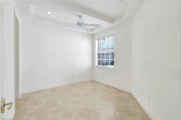 Tiled empty room featuring a raised ceiling and ceiling fan