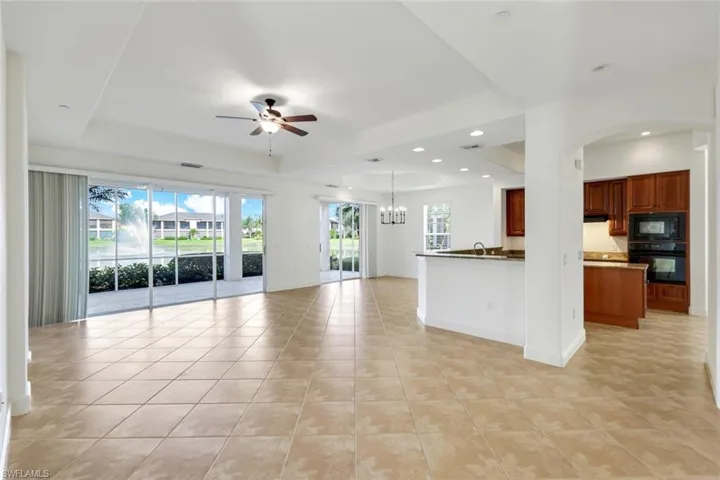 Unfurnished living room with a tray ceiling, sink, light tile patterned floors, and ceiling fan with notable chandelier