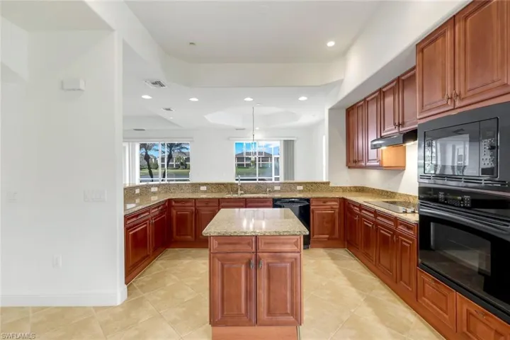 Kitchen with kitchen peninsula, light stone countertops, a raised ceiling, black appliances, and a kitchen island