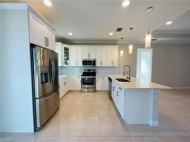 Kitchen with glass insert cabinets, stainless steel appliances, white cabinets, pendant lighting, and light tile patterned floors