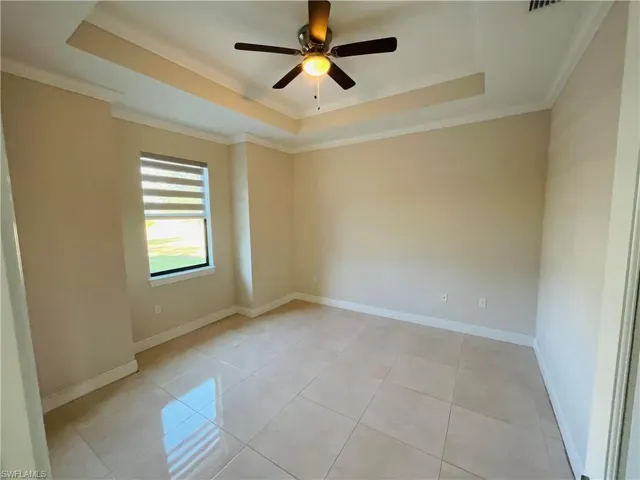Spare room featuring a tray ceiling, ornamental molding, light tile patterned floors, and ceiling fan