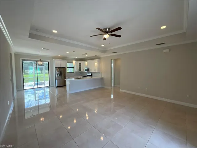 Unfurnished living room featuring a tray ceiling, crown molding, recessed lighting, ceiling fan, and light tile patterned floors