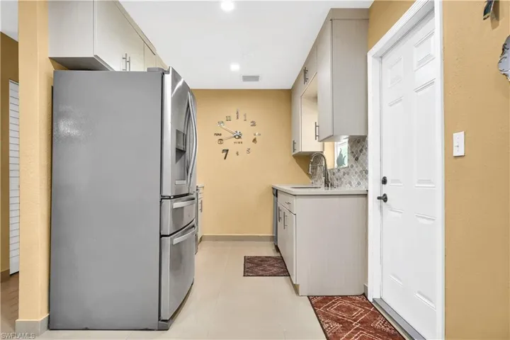 Kitchen with light tile patterned flooring, sink, stainless steel fridge with ice dispenser, and decorative backsplash