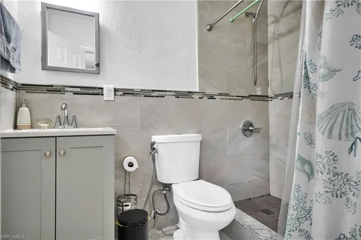 Bathroom featuring walk in shower, vanity, tile walls, and toilet