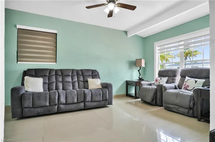 Tiled living room featuring ceiling fan and beamed ceiling