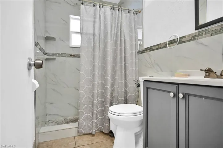 Bathroom with a shower with shower curtain, tile patterned floors, vanity, and toilet