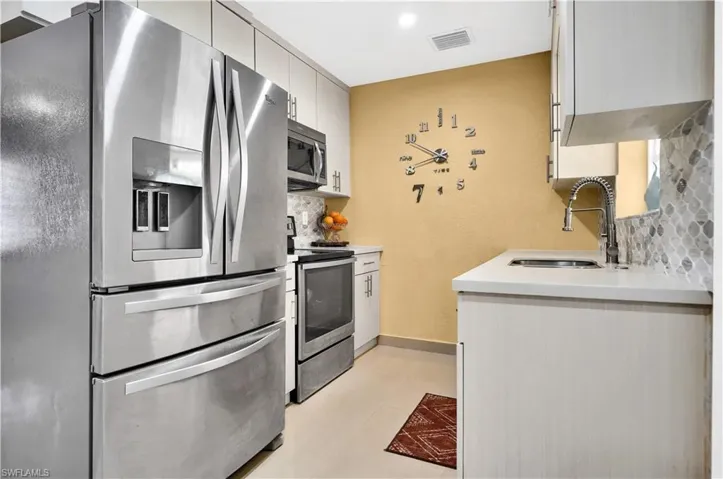 Kitchen with light tile patterned flooring, white cabinets, tasteful backsplash, stainless steel appliances, and sink