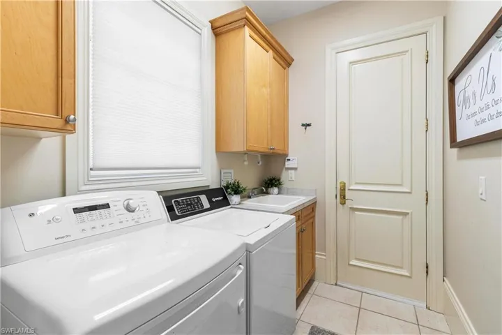 Laundry room with washer and clothes dryer, sink, light tile flooring, and cabinets