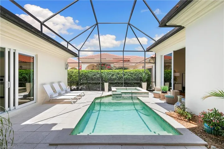 View of swimming pool with glass enclosure, an in ground hot tub, and a patio area