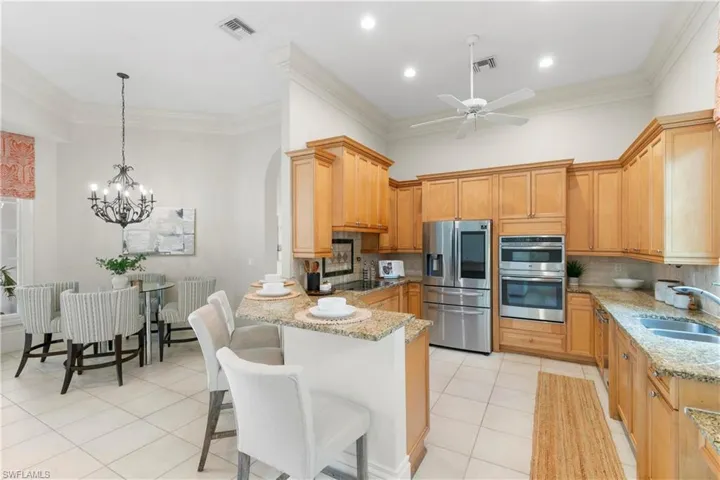 Kitchen featuring ceiling fan with notable chandelier, backsplash, sink, a breakfast bar area, and appliances with stainless steel finishes