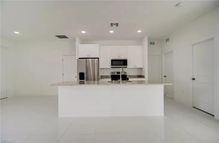 Kitchen with light stone countertops, appliances with stainless steel finishes, an island with sink, white cabinets, and light tile patterned flooring