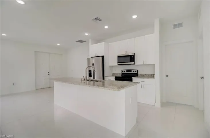 Kitchen featuring a kitchen island with sink, stainless steel appliances, sink, white cabinetry, and light stone counters