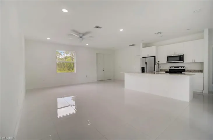 Kitchen with white cabinets, light tile patterned floors, appliances with stainless steel finishes, ceiling fan, and a center island with sink