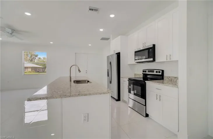 Kitchen featuring light stone countertops, a center island with sink, appliances with stainless steel finishes, sink, and ceiling fan