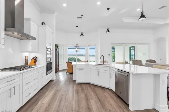 Kitchen with appliances with stainless steel finishes, wall chimney exhaust hood, decorative light fixtures, and white cabinetsVirtually enhanced