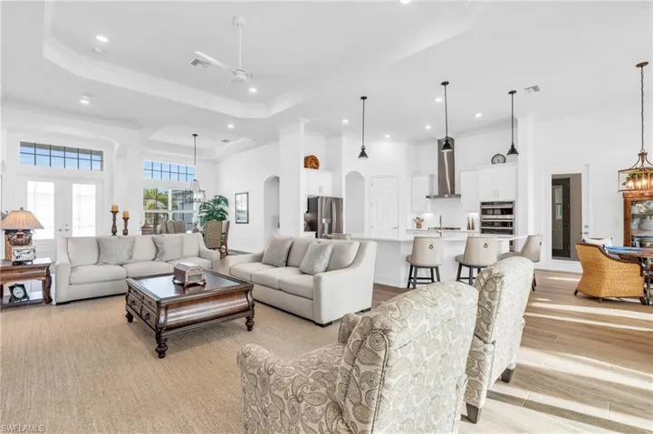Living room featuring ornamental molding, sink, light hardwood / wood-style flooring, a tray ceiling, and ceiling fan with notable chandelierVirtually enhanced