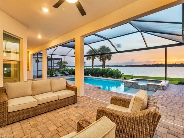 Pool at dusk with a patio area, a water view, an in ground hot tub, glass enclosure, and ceiling fanVirtually enhanced