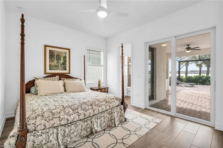 Bedroom featuring wood-type flooring, ensuite bath, ceiling fan, and access to exteriorVirtually enhanced