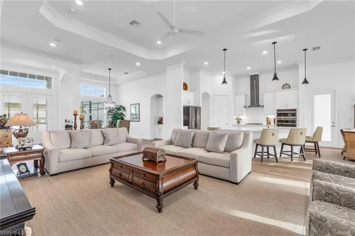Living room featuring ceiling fan with notable chandelier, light wood-type flooring, a raised ceiling, and crown moldingVirtually enhanced