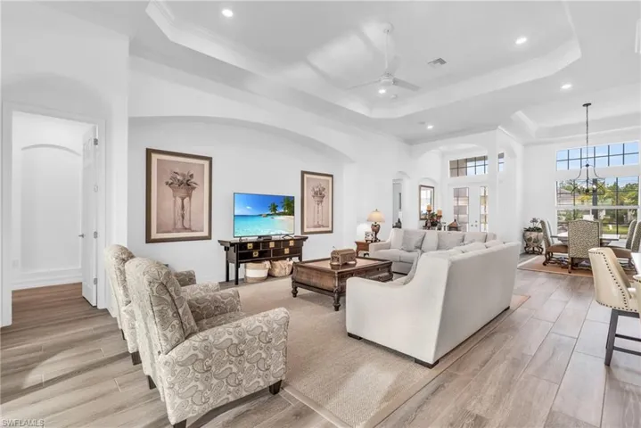 Living room featuring ceiling fan with notable chandelier, light wood-type flooring, crown molding, and a raised ceilingVirtually enhanced