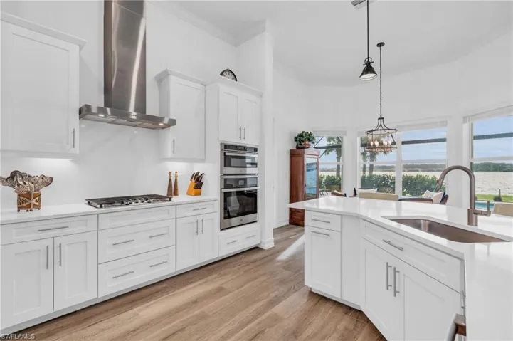 Kitchen with sink, white cabinetry, wall chimney exhaust hood, appliances with stainless steel finishes, and decorative light fixturesVirtually enhanced