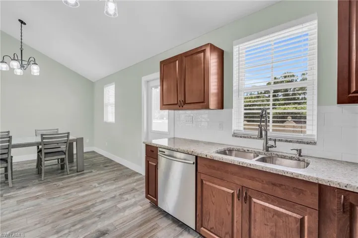 Kitchen with hanging light fixtures, dishwasher, backsplash, light hardwood / wood-style flooring, and a notable chandelier