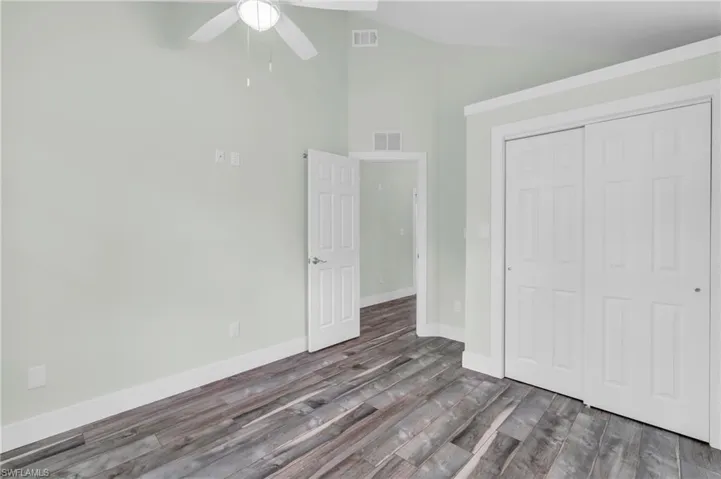 Unfurnished bedroom featuring dark wood-type flooring, vaulted ceiling, ceiling fan, and a closet