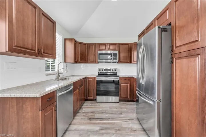 Kitchen featuring light stone counters, stainless steel appliances, light hardwood / wood-style floors, sink, and lofted ceiling