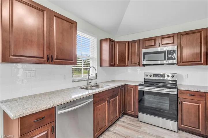 Kitchen featuring light wood-type flooring, stainless steel appliances, sink, light stone countertops, and lofted ceiling