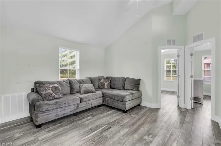 Living room with ceiling fan, light wood-type flooring, and high vaulted ceiling