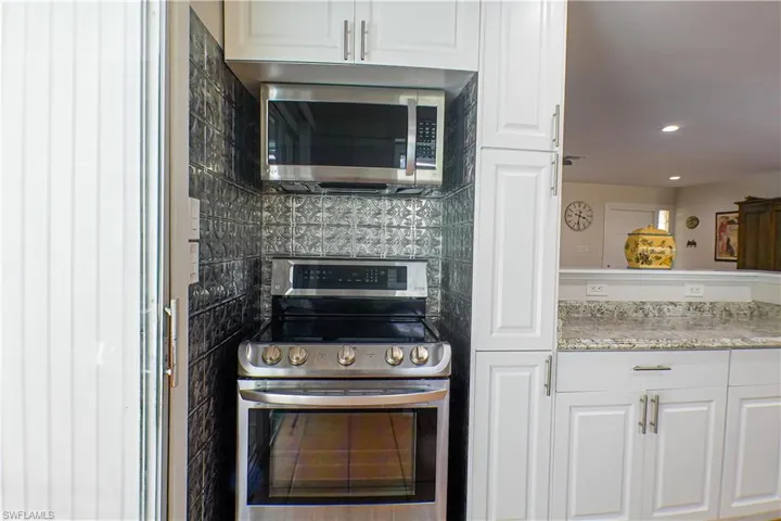 Kitchen featuring white cabinetry, backsplash, light stone counters, and stainless steel appliances