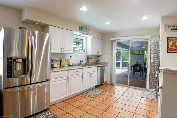 Kitchen with stainless steel appliances, tasteful backsplash, white cabinetry, sink, and tile floors
