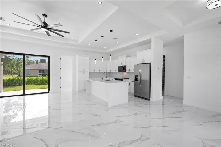 Kitchen featuring white cabinets, stainless steel appliances, an island with sink, open floor plan, and ceiling fan