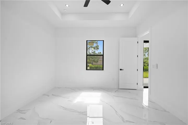 Empty room with healthy amount of natural light, a raised ceiling, a ceiling fan, recessed lighting, and light marble finish flooring