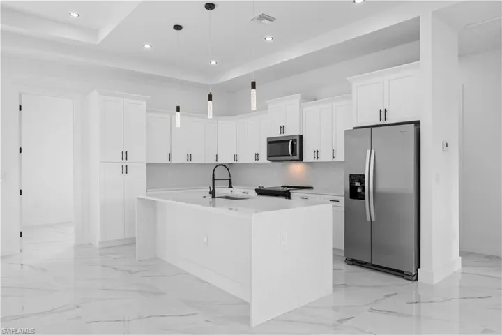 Kitchen featuring stainless steel appliances, light stone counters, white cabinets, a center island with sink, and pendant lighting