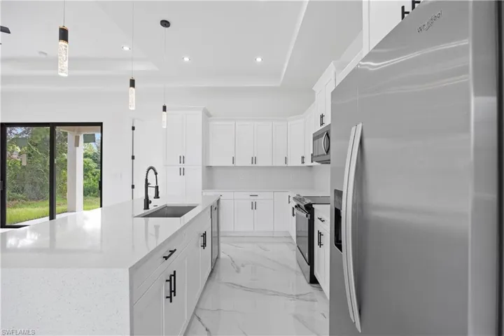 Kitchen featuring stainless steel appliances, white cabinets, light stone countertops, a kitchen island with sink, and a tray ceiling
