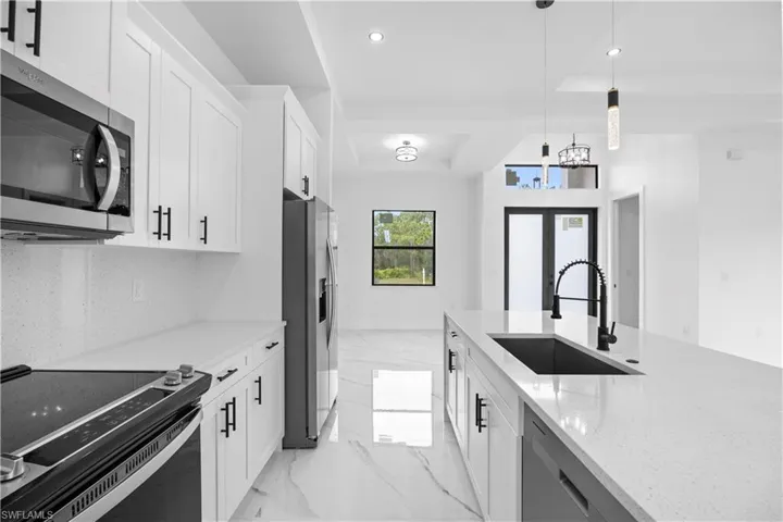 Kitchen featuring stainless steel appliances, white cabinetry, light stone counters, and pendant lighting